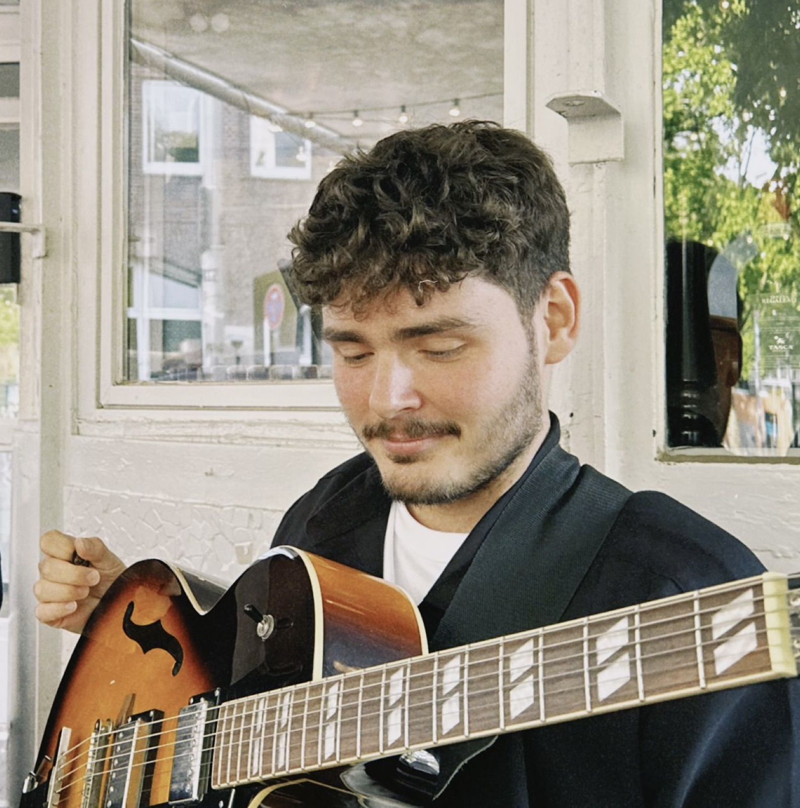 Jonathan Rieske spielt Gitarre vor einem Café-Fenster